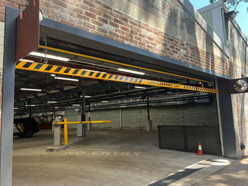 Car park entrance with a yellow-and-black height barrier and automatic boom gate, marked "No Entry," inside a covered parking area.