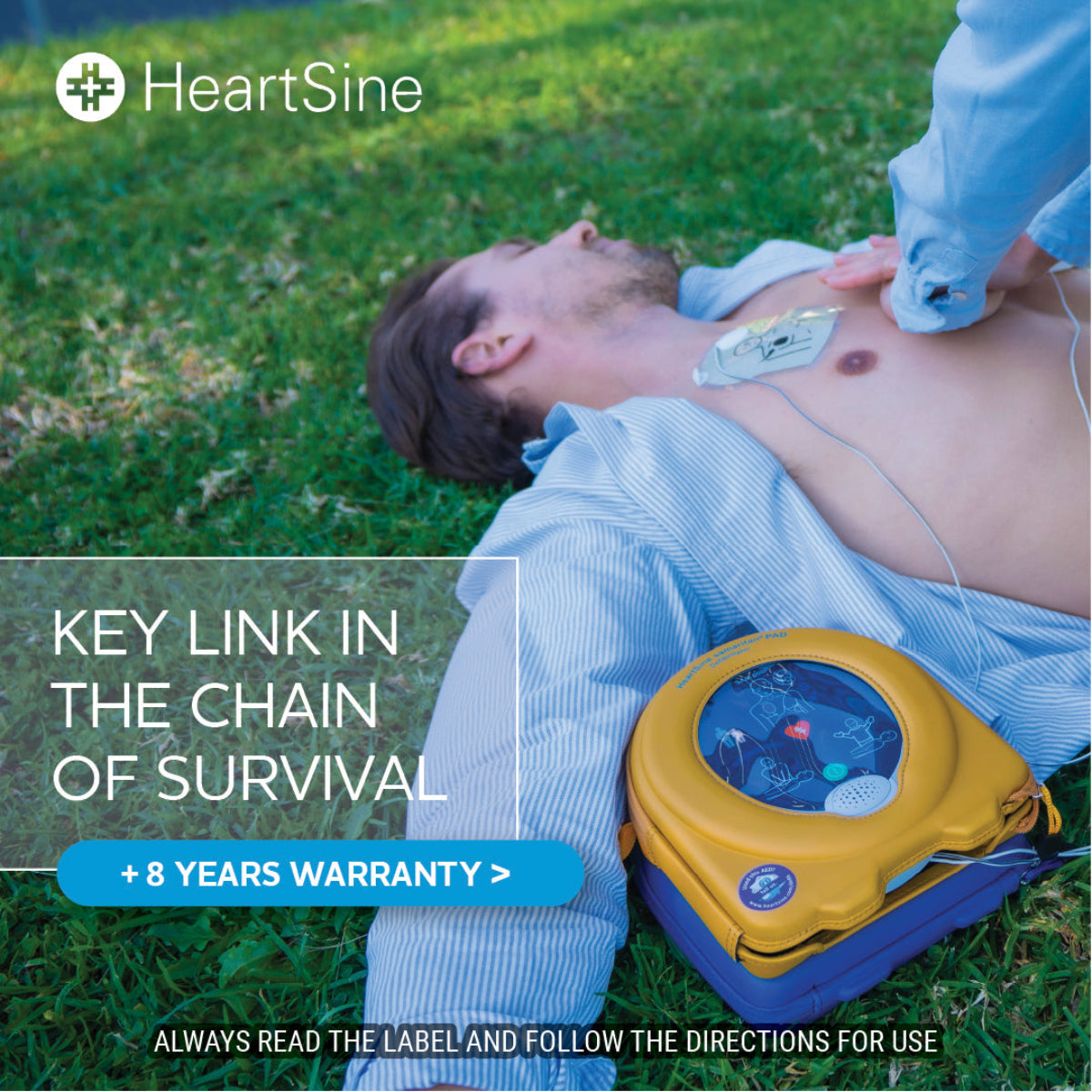 Person receiving CPR with a HeartSine defibrillator on grass, featuring HeartSine branding.