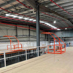 Gas-assisted mezzanine pallet gate in mid-pivot, showing the "up and over" safety design that keeps the platform edge protected during loading.