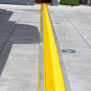 High-visibility yellow PVC-coated foam core drive-over bunding kit laid across a warehouse roller door threshold for spill containment.