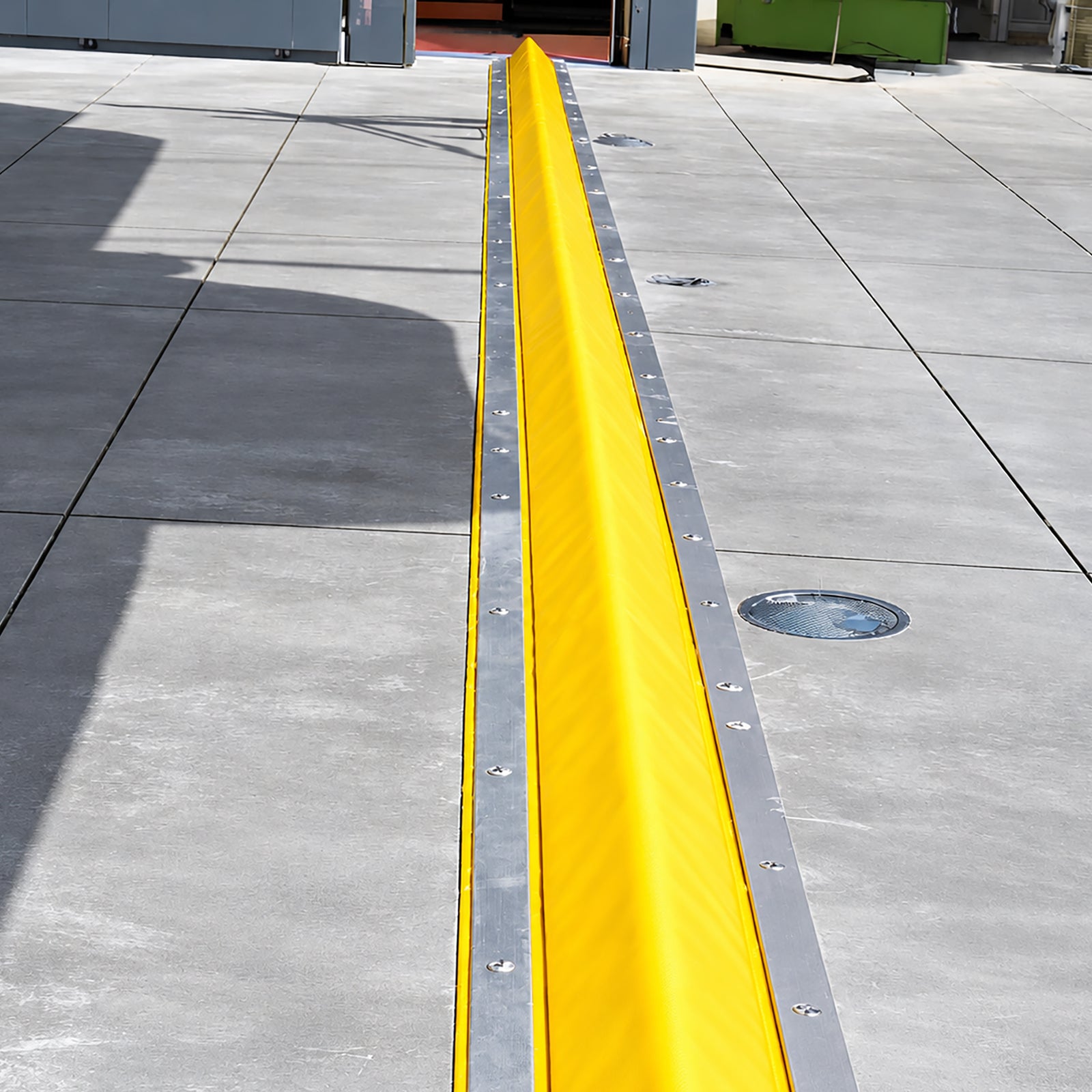 High-visibility yellow PVC-coated foam core drive-over bunding kit laid across a warehouse roller door threshold for spill containment.